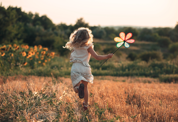 Kind mit Blume springt im Feld 